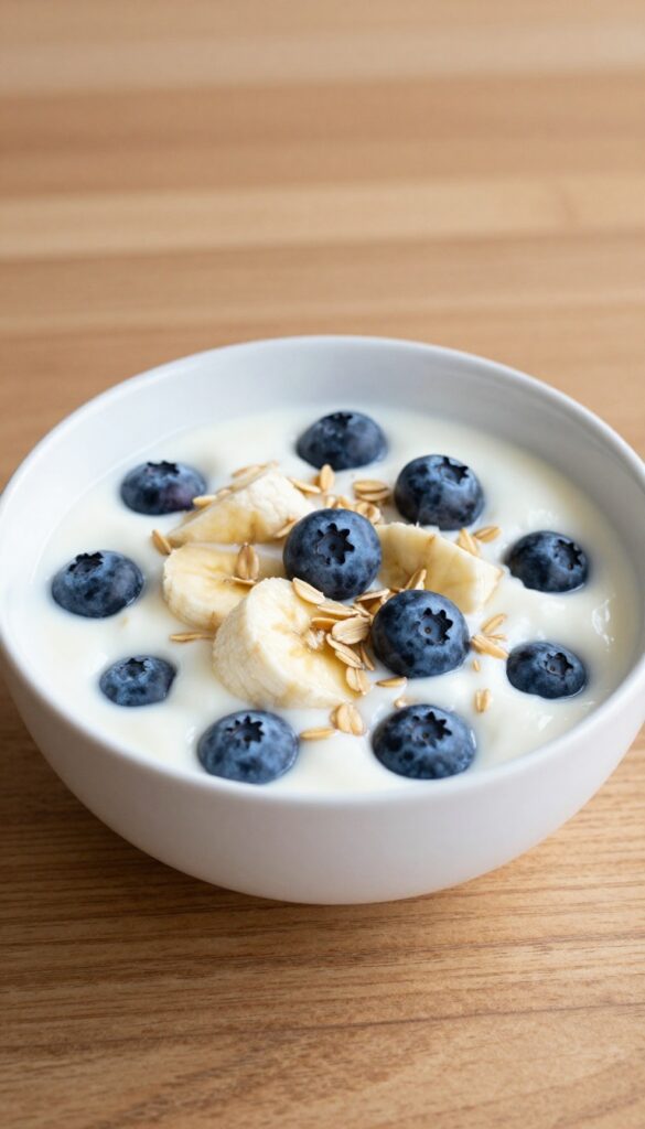 A bowl of yogurt mixed with oats, blueberries, and banana pieces, representing a homemade cooling dog treat recipe.