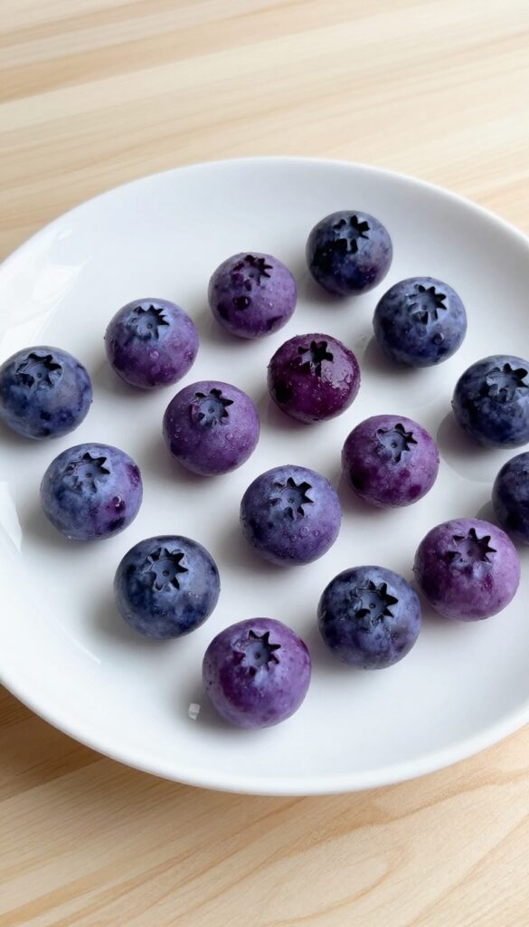 Frozen yogurt blueberry drops for dogs, arranged on a white plate with a wooden background, showcasing homemade dog treats in natural light.