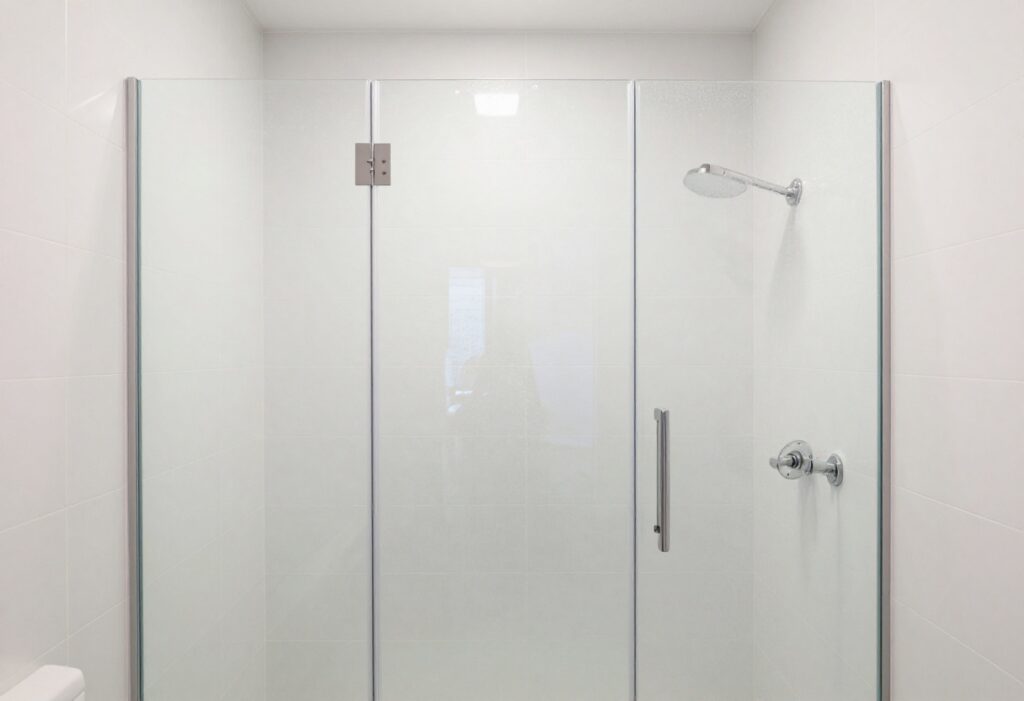 A sparkling clean shower with clear glass doors and spotless white tiles