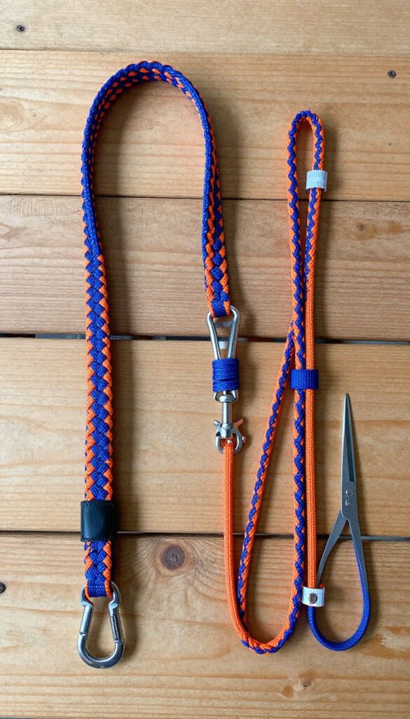 Partially braided paracord dog leash on wooden table with supplies