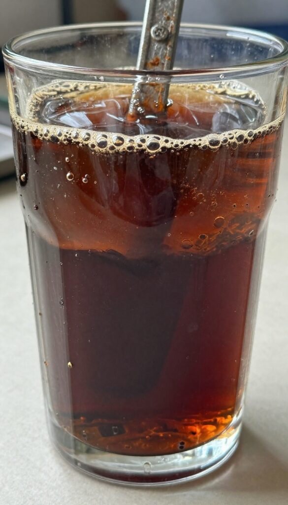 Rusty wrench soaking in cola in a glass container, DIY rust removal method.