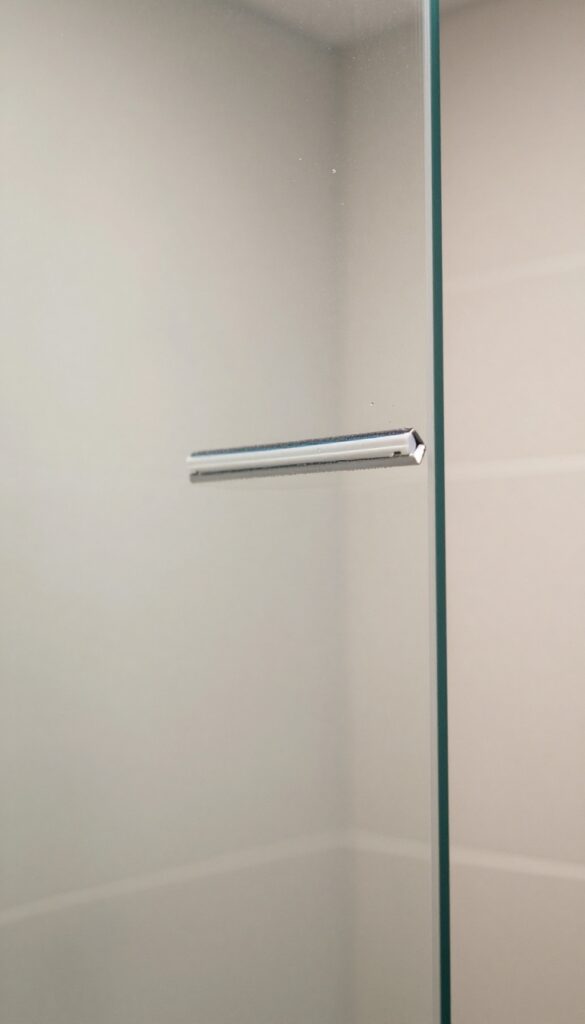 Clean glass shower door with a squeegee, bright natural light, streak-free surface, tiled background